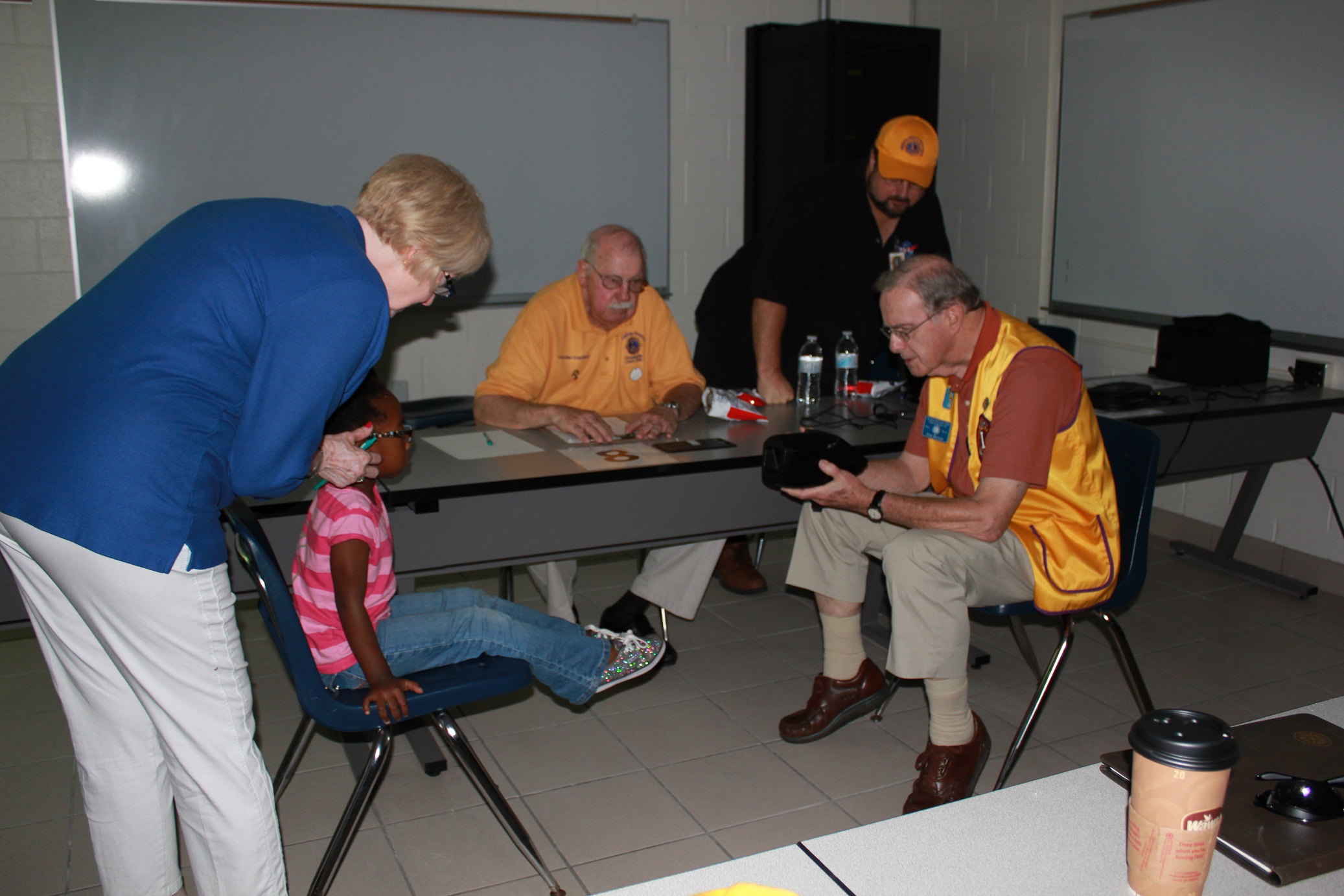 Lions James “Jim” Palacio, Jr., John Cranford and Don Beuson administer a vision test and help Marquesa W. to adjust her glasses to be sure they get an accurate reading.
